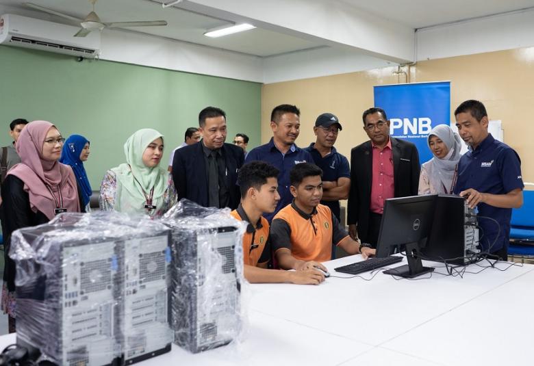 Mohd Hassany (kanan) meninjau pelajar yang sedang mencuba komputer sumbangan PNB di Kelantan.