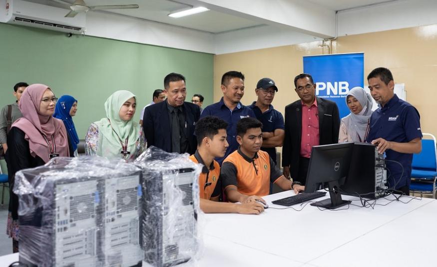 Mohd Hassany (kanan) meninjau pelajar yang sedang mencuba komputer sumbangan PNB di Kelantan.